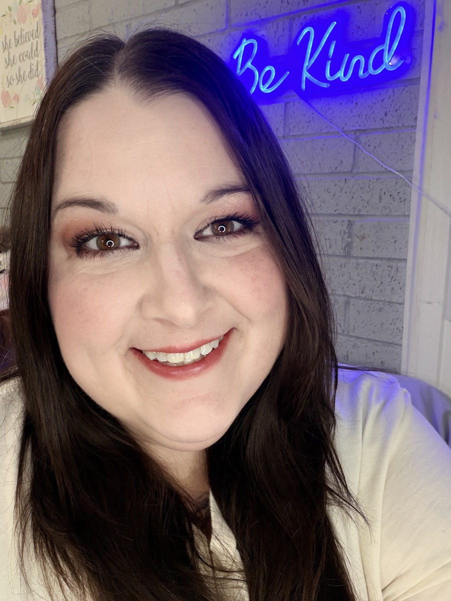 Mandy, 116 pounds down after her Emerge Weight Loss journey, smiling in front of a Be Kind sign